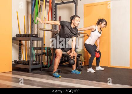 Woman and man doing shoulder press exercises with kettlebells in gym. Stock Photo