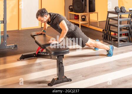 Adult man doing push ups on bench in the gym Stock Photo