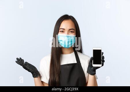 Covid-19 pandemic, coffee shop, small business and preventing virus concept. Smiling cute asian female barista showing cafe application on smartphone Stock Photo