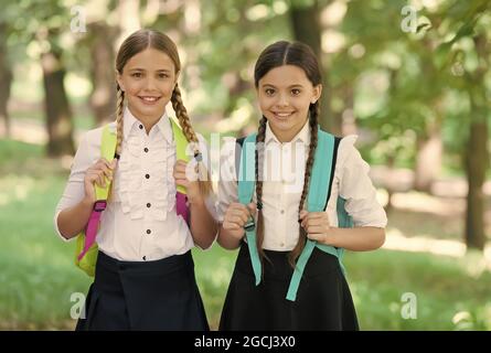 Playful mood. Fashion little girls with backpack in park. children with backpack smiling. students outside in summer park smiling happy. girls with Stock Photo