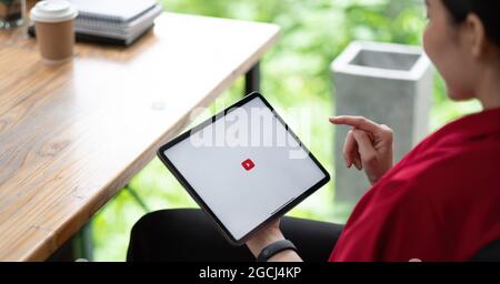 CHIANG MAI, THAILAND - AUG 01, 2021 : Woman hand holding and is pressing the Youtube screen on apple digital tablet, YouTube is the popular online Stock Photo