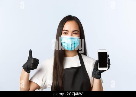 Covid-19 pandemic, coffee shop, small business and preventing virus concept. Smiling attractive asian cafe owner, barista showing smartphone screen Stock Photo