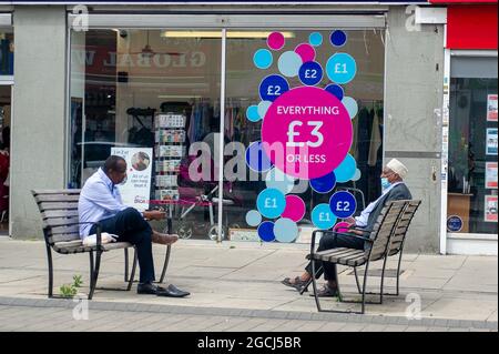 Hayes, London Borough of Hillingdon, UK. 5th August, 2021. Men wearing face masks sit and chat outside a charity shop. Shoppers were out and about in Hayes town centre today. Many continue to wear face masks whilst they are shopping. Credit: Maureen McLean/Alamy Stock Photo