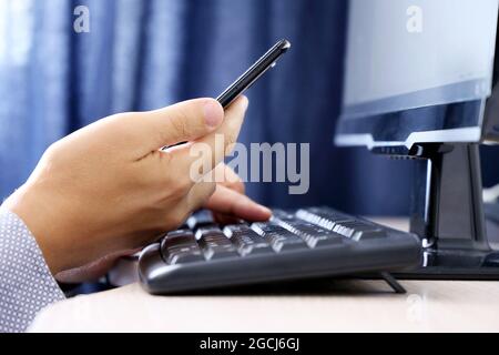 Man using smartphone on PC keyboard background. Concept of online communication, office or home work and payment Stock Photo