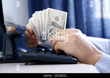 US dollars in male hands. Man pulls money out of an envelope on PC keyboard background, wages, bonus or bribe concept Stock Photo