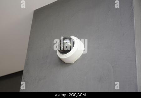 A close-up of a round security camera, security surveillance installed on a gray plastered wall inside a modern apartment. Stock Photo