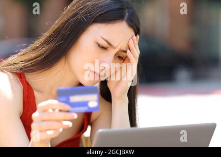 Worried woman having problems buying online with credit card and laptop in the street Stock Photo
