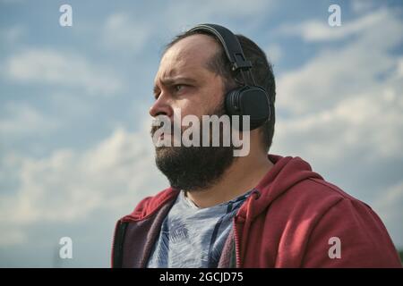 Middle-aged European man in headphones outdoors listening to music against the background of the sky Stock Photo