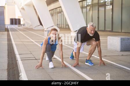 Sportive middle aged couple getting ready to start the sprint, running outdoors in urban environment Stock Photo