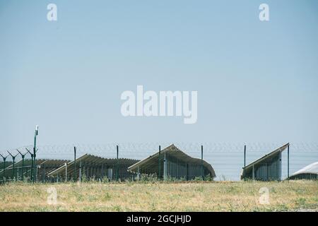 Multiple rows of solar panels behind a fence. Side view. Clear blue sky over them. Stock Photo