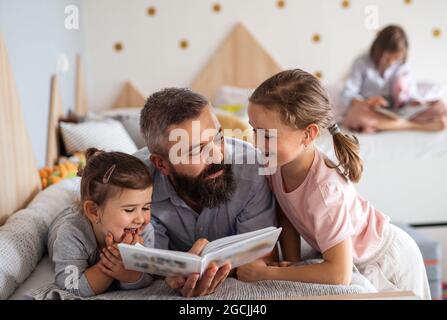 Father with three daughters indoors at home, reading a book. Stock Photo