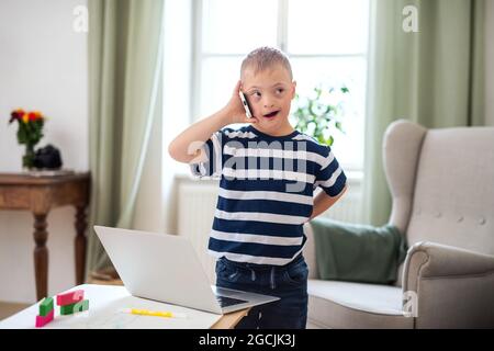 Happy down syndrome son indoors at home, using smartphone. Stock Photo