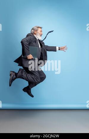 Scared professor, teacher, gray-headed bearded man running, hurrying to class isolated on blue studio background. Funny meme emotions Stock Photo