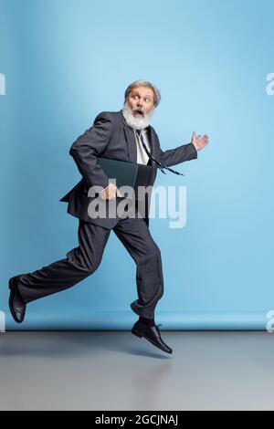 Scared professor, teacher, gray-headed bearded man running, hurrying to class isolated on blue studio background. Funny meme emotions Stock Photo