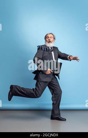 Scared professor, teacher, gray-headed bearded man running, hurrying to class isolated on blue studio background. Funny meme emotions Stock Photo