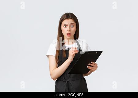 Grocery store employees, small business and coffee shops concept. Confused woman writing on clipboard and stare camera frustrated, having trouble with Stock Photo