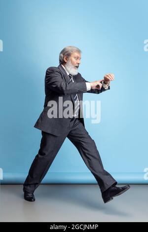 Scared professor, teacher, gray-headed bearded man running, hurrying to class isolated on blue studio background. Funny meme emotions Stock Photo