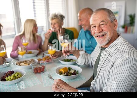 Senior man with friends having party indoors, eating at the table. Stock Photo