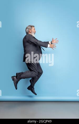 Scared professor, teacher, gray-headed bearded man running, hurrying to class isolated on blue studio background. Funny meme emotions Stock Photo