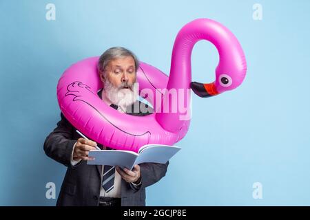 Portrait of elder gray-headed man, professor, teacher working isolated on blue studio background. Concept of professional occupation, job, education Stock Photo