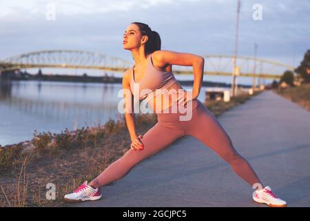 Young Caucasian jogger woman stretching legs before run at riverside Stock Photo