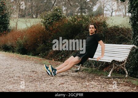 Young Caucasian guy doing fitness stretching on a bench in a park Stock Photo