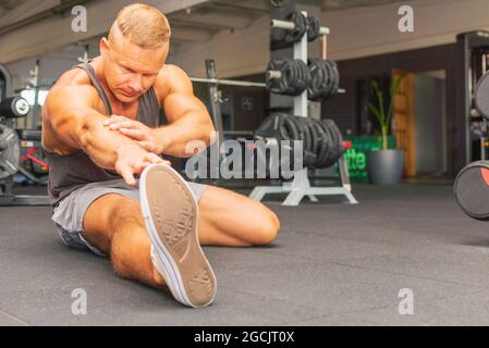 Man at the gym doing stretching exercises on the floor.Sports man at the gym doing stretching legs feet exercises. Stock Photo