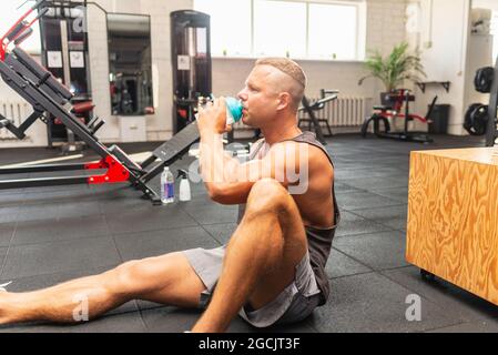 Young caucasian man drinking water after exercise.man in the gym drinking from the shaker.Muscular Man Resting After Exercise And Drinking From Shaker Stock Photo