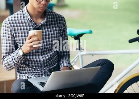 Cropped image of serious software developer sitting on bench in park, drinking coffee and working on new big project Stock Photo