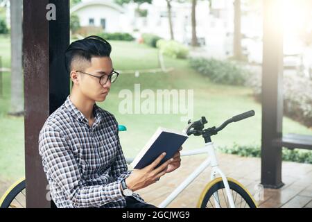 Serious pensive young man reading students book on university campus getting ready for exam Stock Photo