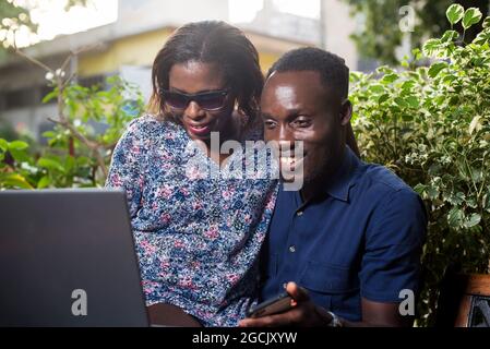 young couple sitting in a park looking at laptop smiling. Stock Photo