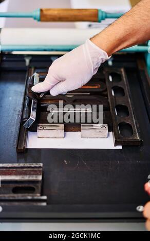 Crop unrecognizable craftsman making imprint of metal letters on paper while working in printing workshop Stock Photo