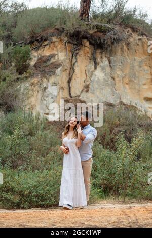Happy diverse bride and groom embracing while standing in forest on wedding day Stock Photo