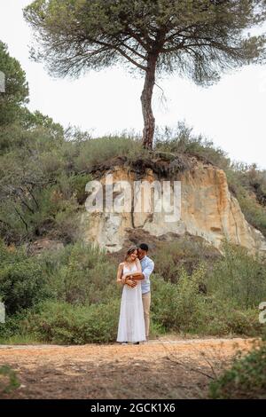 Happy diverse bride and groom embracing while standing in forest on wedding day Stock Photo