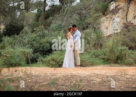 Diverse bride and groom embracing while standing in forest on wedding day Stock Photo