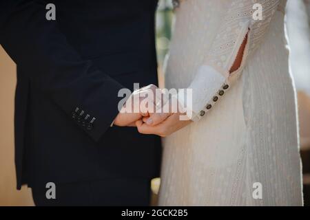 Crop side view of anonymous groom holding hands of elegant bride in white wedding gown Stock Photo