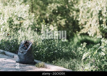 Black garbage bag placed on pathway after collecting trash in green park in summer day Stock Photo