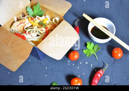 Noodles with pork and vegetables in take-out box on wooden table Chinese noodles with vegetables. Ingredients in box: noodles, chicken meat, mushrooms Stock Photo