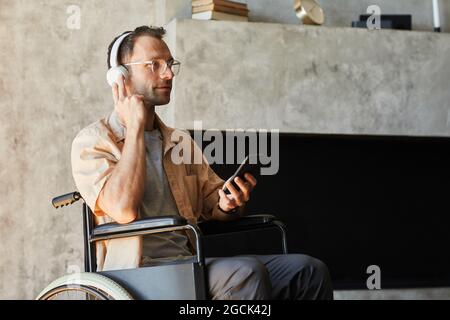 Portrait of disabled modern man in wheelchair listening to music at home, copy space Stock Photo