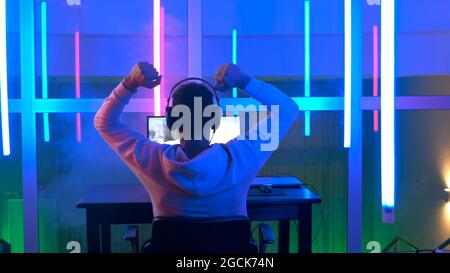 Back view of young gamer winning online game. He playing on his personal computer in neon room. Stock Photo