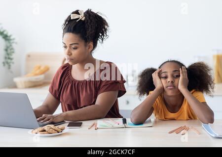 Black woman freelancer working from home, bored daughter sitting by Stock Photo