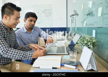 Team of UI and UX designers discussing document with website interface layout and choosing what to add and what to change Stock Photo