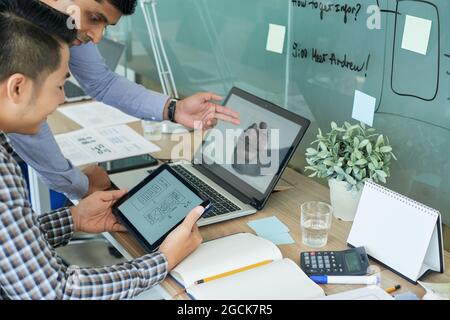 Team of UI designers working on interface of new mobile application and comparing layouts on screen of tablet computer and laptop Stock Photo