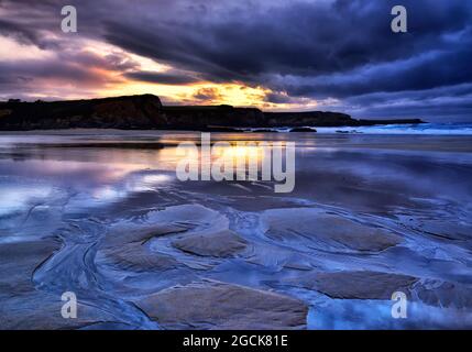 Spectacular scenery of wet beach and calm sea under sundown sky in evening Stock Photo