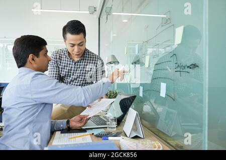 UX and UI designers working on project together, they are discussing chart on glass wall and documents with interface layouts Stock Photo