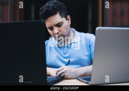 Man writing down data on a paper while trading cryptocurrencies with laptops Stock Photo