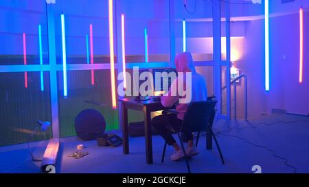 Hacker working place: hacker working in a room with colored neon lights. He writing hacker program. Hooded Hacker Breaks into Government Data Servers. Stock Photo