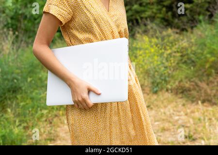 Crop anonymous female freelancer holding laptop while standing in summer park Stock Photo