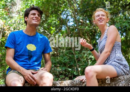 Young couple sitting on wall in front of trees Stock Photo