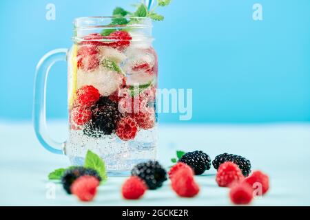 Fresh berries cocktail in glass jar. Fresh summer cocktail with mix of berries, lemon and mint on blue background. Party, drink, summer concept Stock Photo